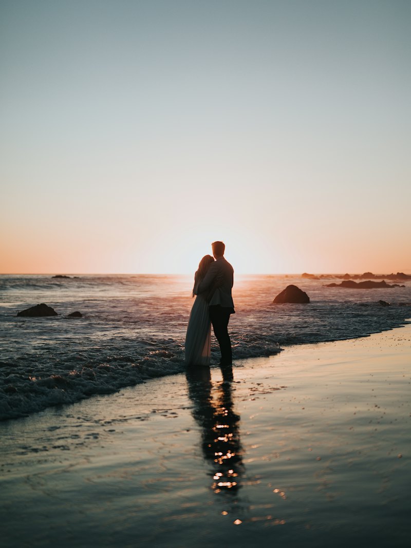 Casal abraçado na praia observando o pôr do sol